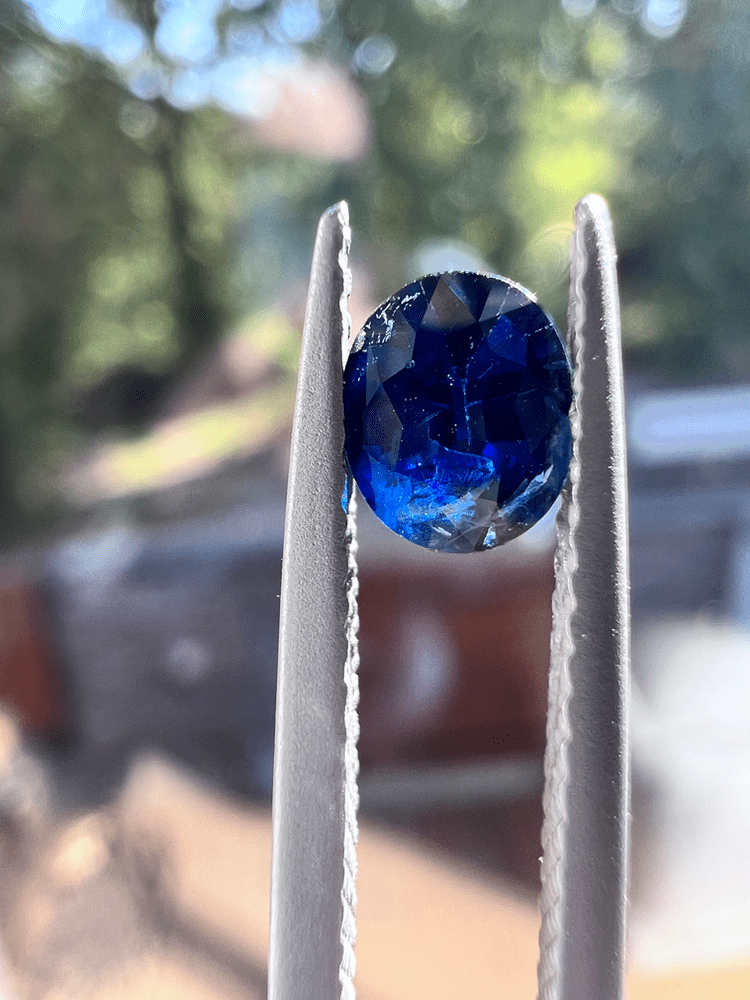 pierre bleue de saphir sur fond neutre tenue par des brucelles (pinces gemmologiques)pour illustrer une pierre bleue. ce traitement fait partie des traitements les plus courants