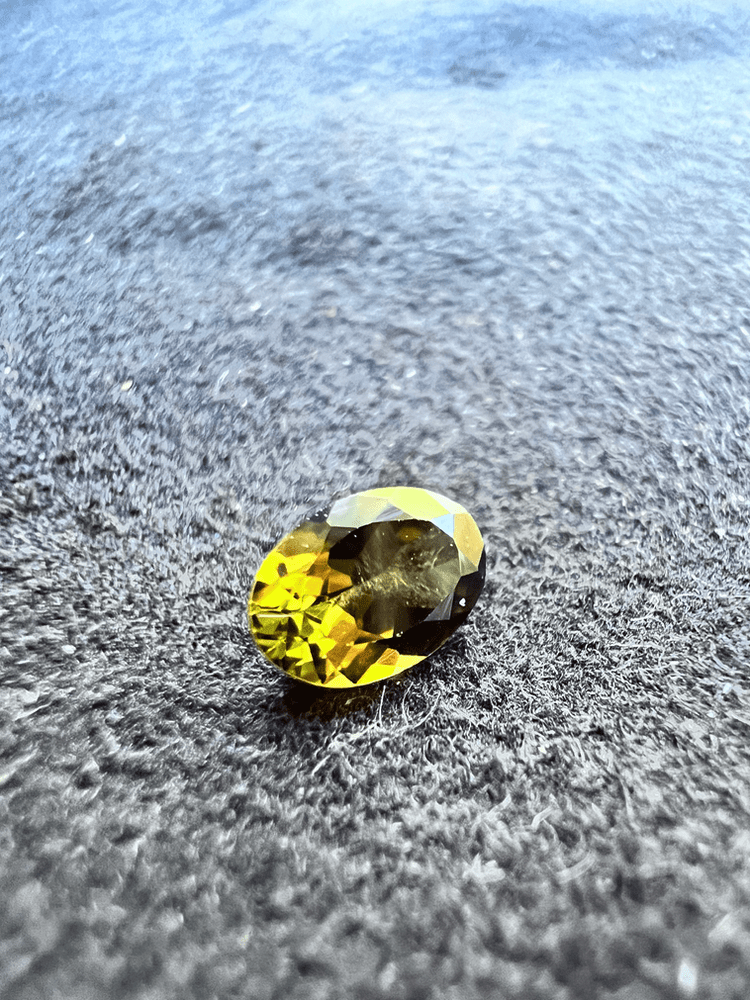 pierre jaune de saphir diffusé au berrylium sur fond neutre tenue par des brucelles (pinces gemmologiques)pour illustrer une pierre jaune