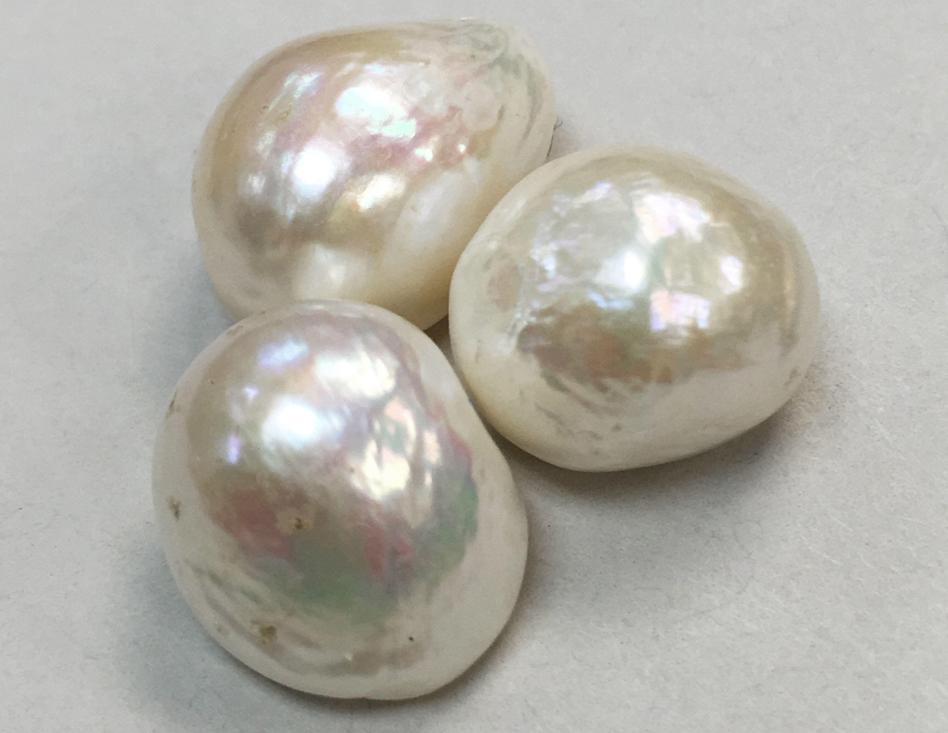 trois perles naturelles blanc rosé sur fond blanc montrant leur forme baroque pour illustrer les parles naturelles