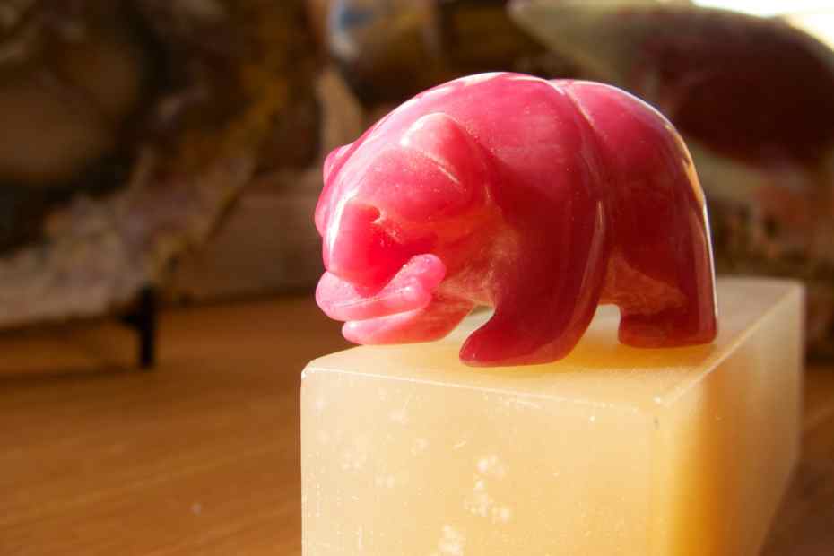 ours sculpté en rhodonite rose translucide sur bloc blanc crème pour illustrer la rhodonite