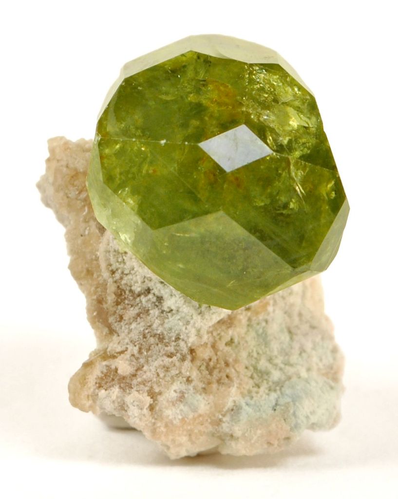 cristal de grenat démantoïde vert avec ses facettes naturelles et posé sur sa roche initiale beige claire