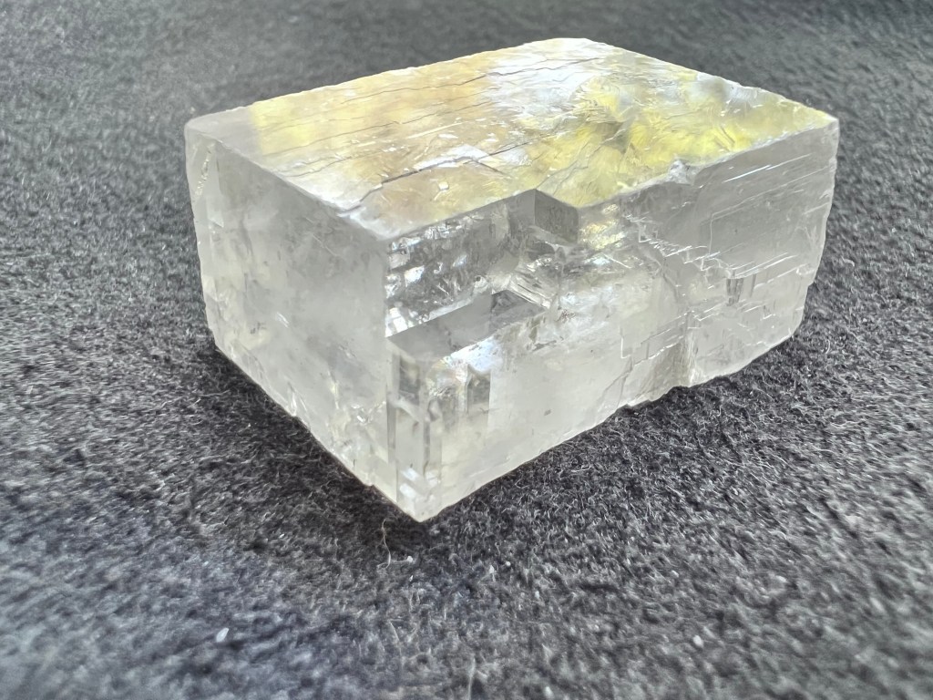 cristal de calcite brut de forme presque rectangulaire et transparente sur fond gris pour illustrer la calcite