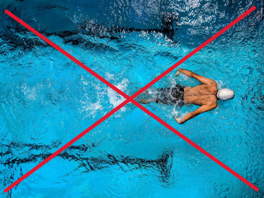 piscine municipale vue du dessus avec l'eau bleue claire et un nageur masculin faisant du papillon pour illustrer les gemmes à ne pas porter à la piscine