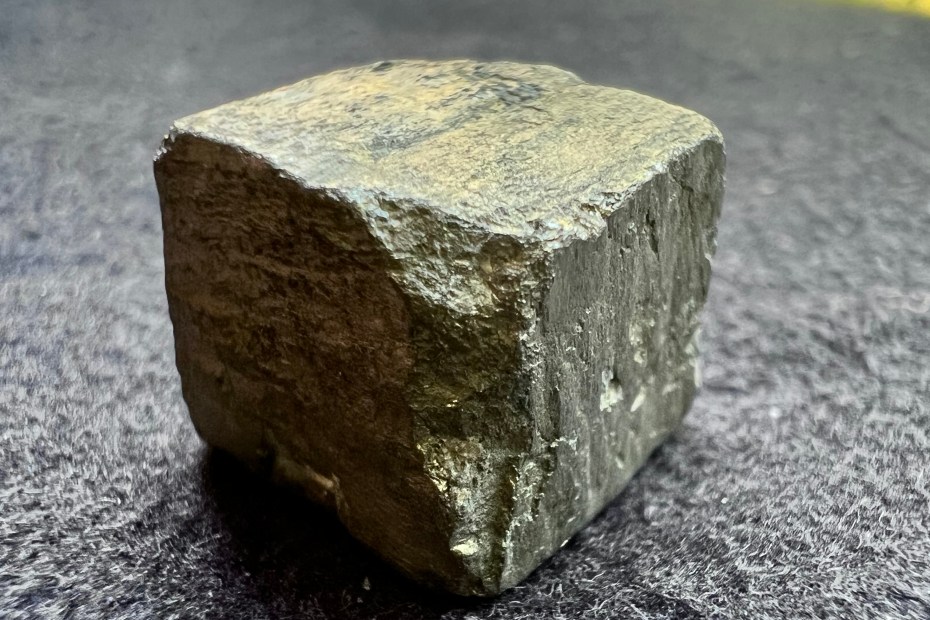 cristal de pyrite naturelle en forme de cube montrant sa couleur metallique doré sur fond de tissu gris pour illustrer la pyrite