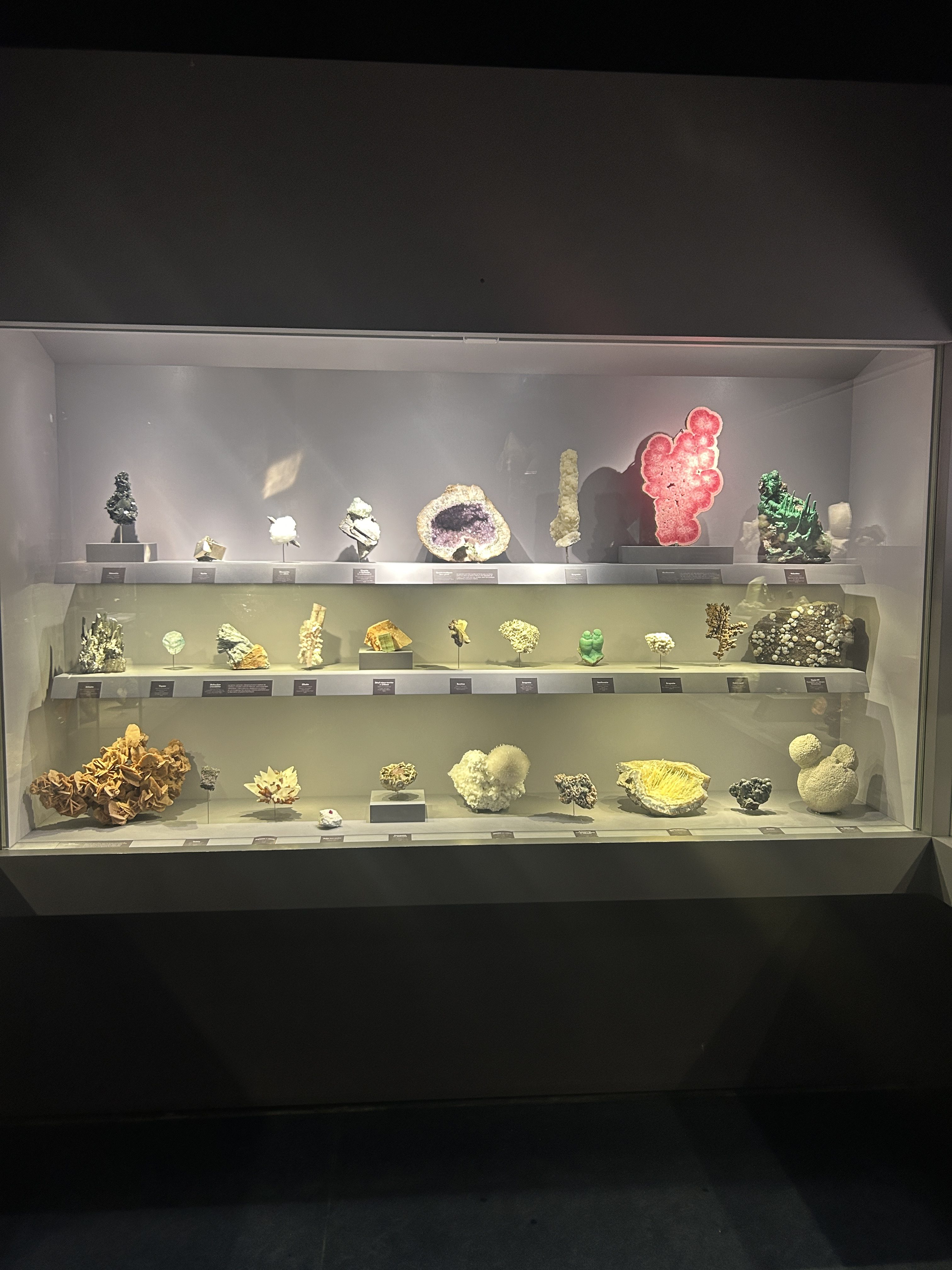 Vitrine du musée montrant une trentaine de pierres différentes de toutes les couleurs, dont la tranche de rhodochrosite. Exposé au musée.